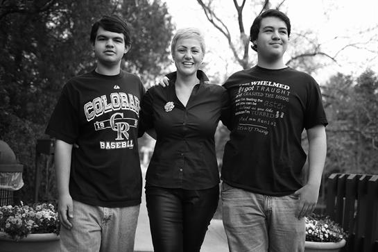 A woman and her two sons stand together in a park, smiling and enjoying the day.