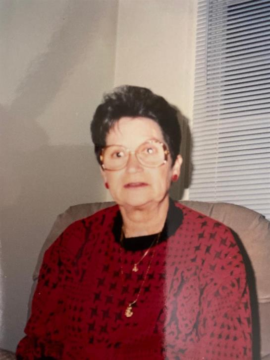 A woman in a red patterned sweater rests in a chair, gazing thoughtfully with glasses on.