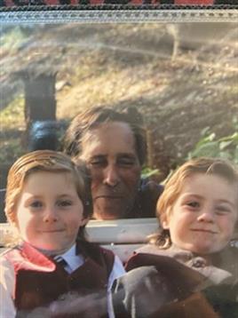 Two children pose happily with an older man in a lush outdoor area, enjoying their time together.