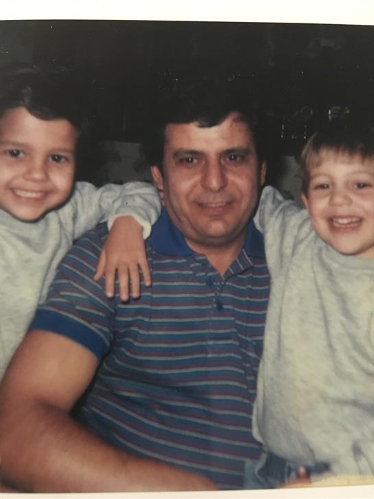 Two smiling kids lean against a man, all in matching outfits, radiating joy and warmth.
