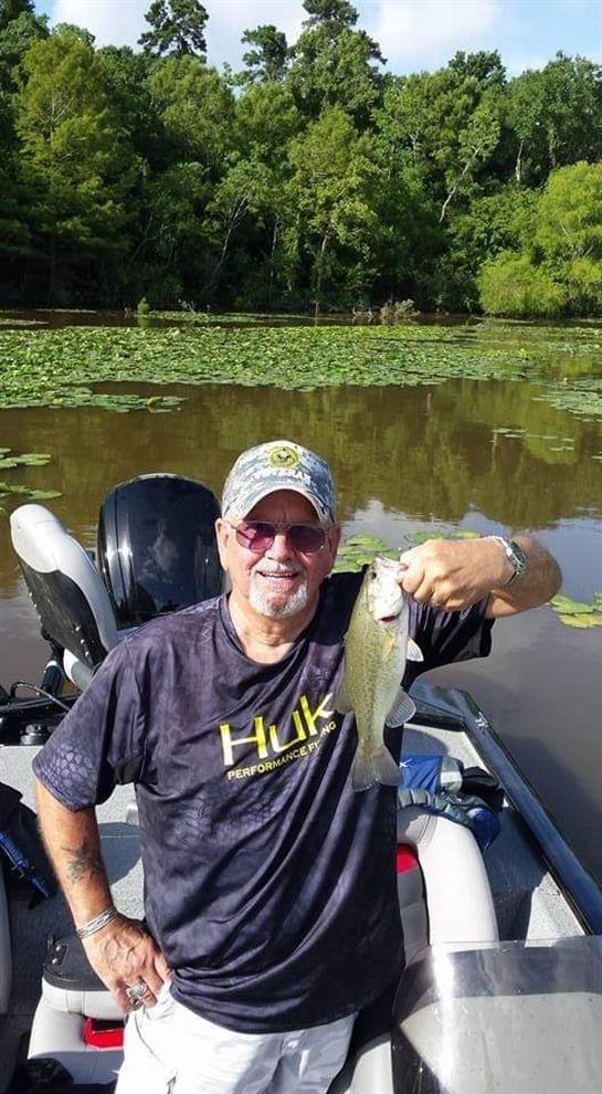 A senior man smiles as he shows off a caught fish while sitting in a boat on a peaceful lake.