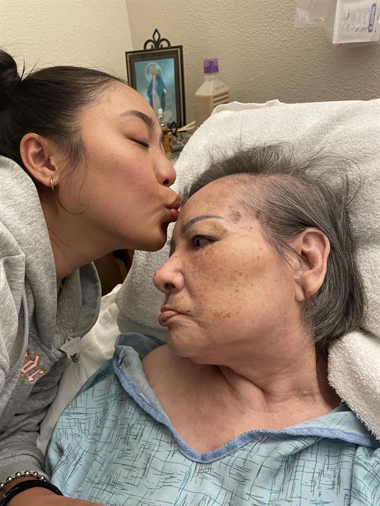 A young woman kisses an elderly woman on the forehead, showcasing love and care.
