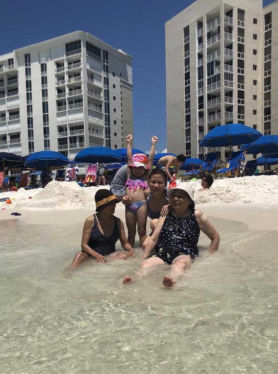 Families play together in shallow waters, surrounded by beach umbrellas on a bright sunny day.
