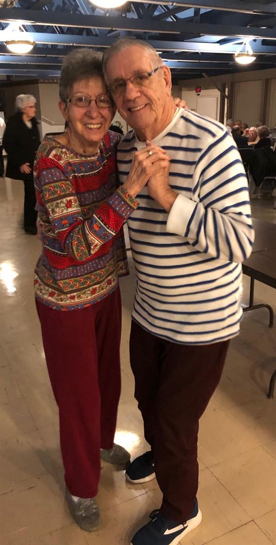 Two seniors share a joyful dance, savoring companionship at a lively event.