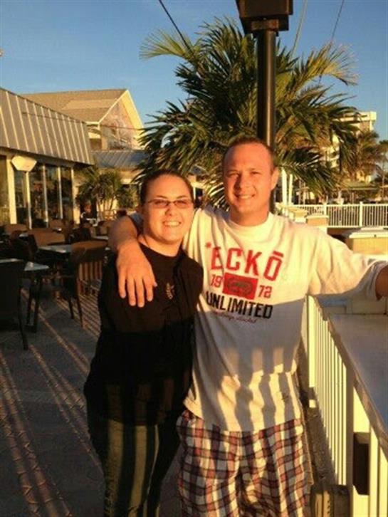 Happy couple poses together at sunset near a lively waterfront restaurant.