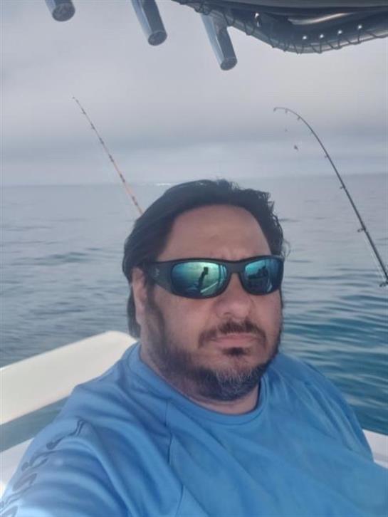 Person relaxes on a boat during a fishing outing, enjoying the calm water and clear sky.