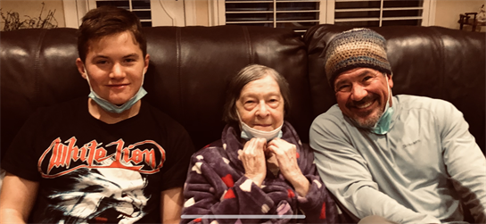 Two adults and an elderly woman interact happily while seated on a couch at home.
