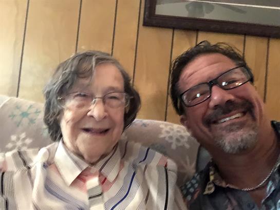 A joyful elderly woman and man take a close-up selfie while sitting on a couch at home.