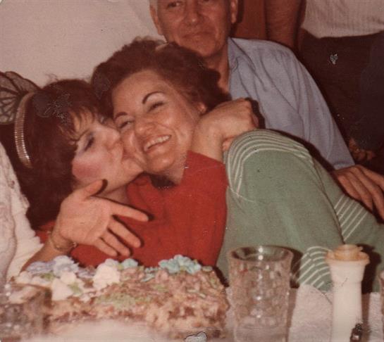 Two friends share a warm embrace and kiss while celebrating a birthday with cake.