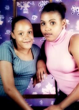 Two women are smiling and posing for a portrait against a vibrant floral backdrop.