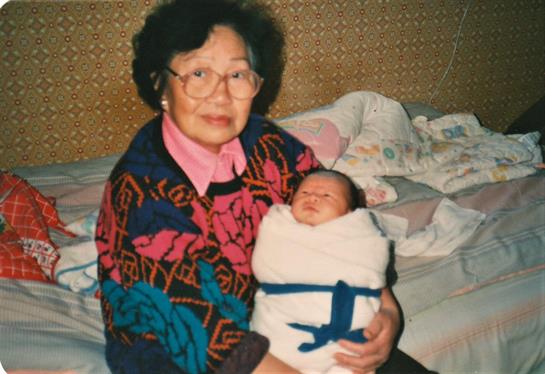 Grandmother gently holds her wrapped newborn grandchild in a warm and loving embrace indoors.