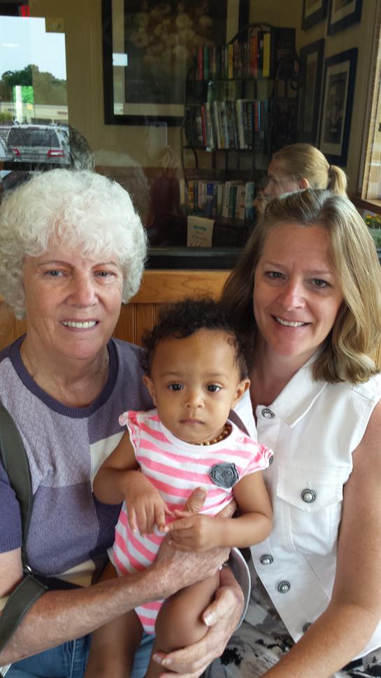 Three family members, including a toddler, share smiles and warmth at a cafe on a sunny day.