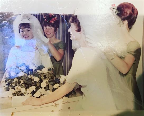A bride gazes into a mirror, surrounded by friends, flowers, and joyful vibes before the ceremony.