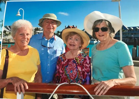 Four friends smile while posing together on a boat railing under clear skies.