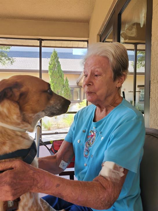 Elderly woman shares a loving gaze with her dog while sitting at a cafe outside on a sunny day.