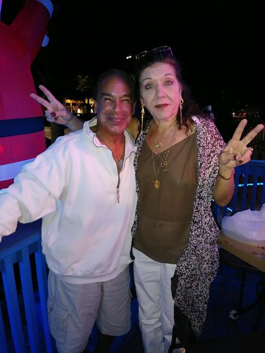 Two friends pose happily on a deck, making peace signs amid vibrant decorations at night.