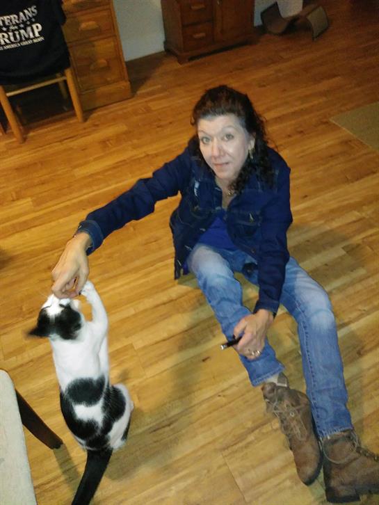 Individual sits on the wooden floor while engaging with a curious black and white cat.