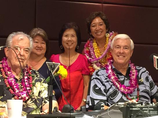 A group of friends poses joyfully in Hawaii, adorned with colorful leis and vibrant clothing.