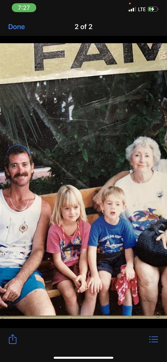 A family sits together on a bench surrounded by greenery, sharing joyful moments with children.