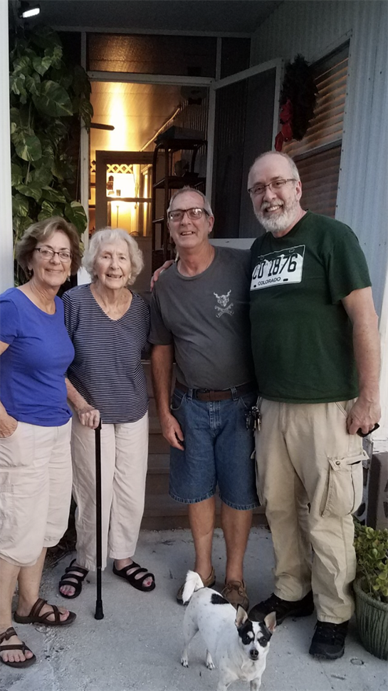 Four friends smile together on a porch during a warm evening, enjoying each other's company.