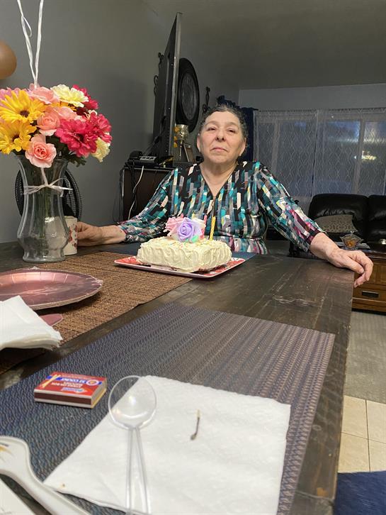 An elderly woman enjoys a cake at a family celebration in a cozy living room.