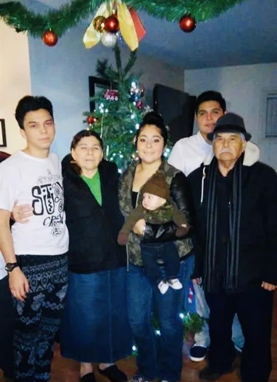 Family members gather around a Christmas tree, celebrating together in a warm atmosphere.