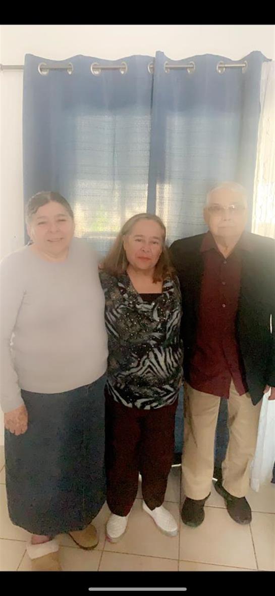 Three family members stand together, smiling warmly in a comfortable indoor environment.