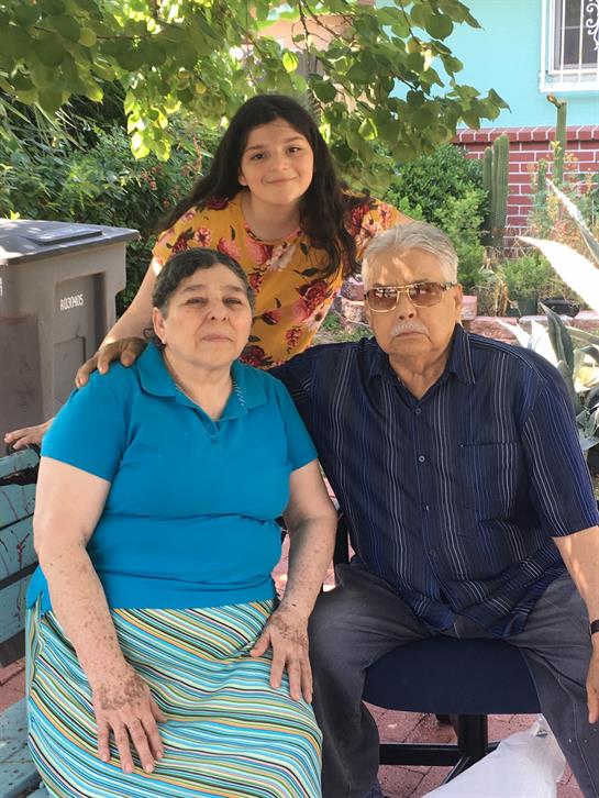 Three family members pose happily in a garden, enjoying quality time together in the warm sunlight.