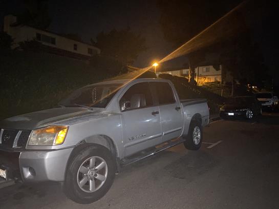 A silver pickup truck is parked under streetlights on a quiet urban street at night.
