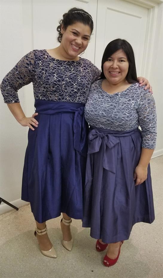 Two women in matching elegant blue dresses stand side by side, smiling happily.