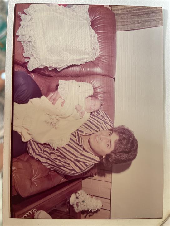 A woman holds a newborn baby while sitting on a couch in a warm family setting.