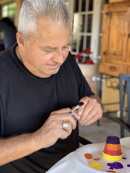 An older man is intently working on a craft project using various supplies at a well-lit table.