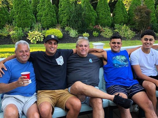 Five relatives relax on a bench in the backyard, sharing laughs and drinks during a summer day.