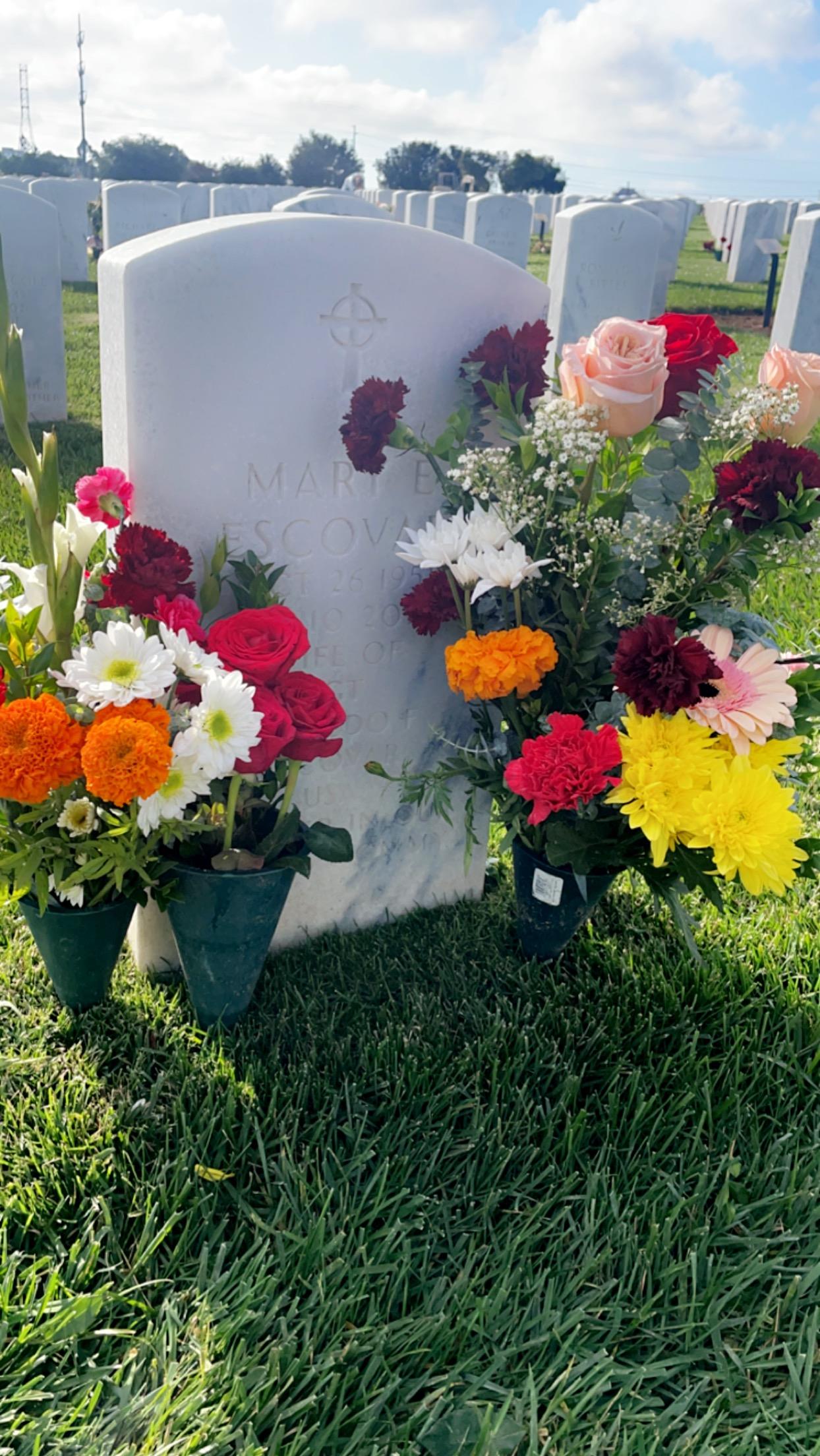 Brightly colored flowers are arranged at a gravestone in a peaceful cemetery setting.