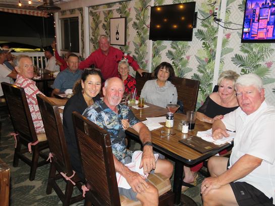 Friends gather around tables to share laughs and meals in a vibrant tropical setting.