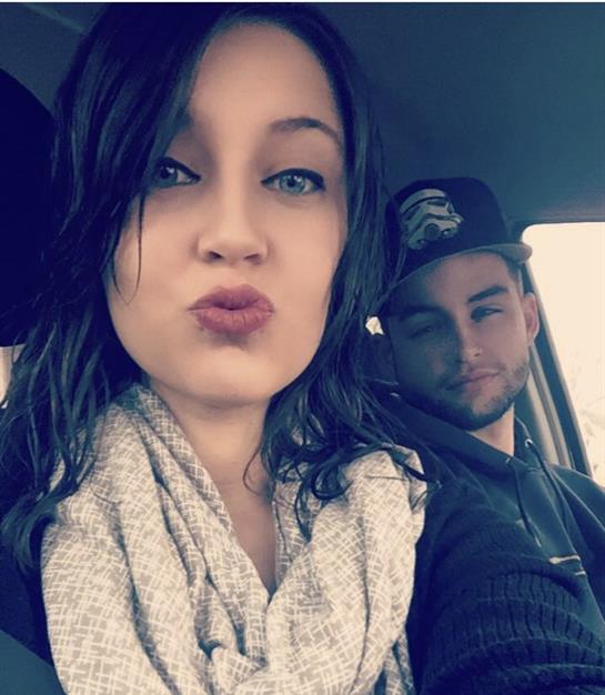 A young couple shares a playful moment inside their car on a cloudy day, smiling at the camera.