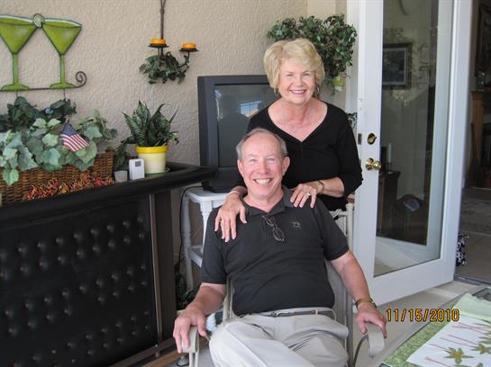 Two smiling individuals share a cheerful moment in an inviting garden space surrounded by plants.