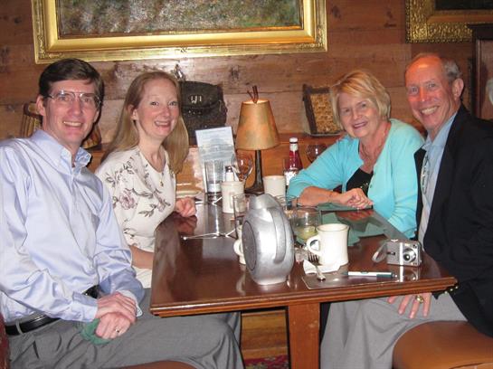 Four friends gather around a table, exchanging stories and laughter in a warm setting.
