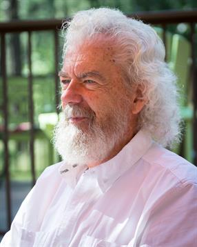 Calm elderly man with curly white hair gazes contemplatively outdoors in a peaceful environment.