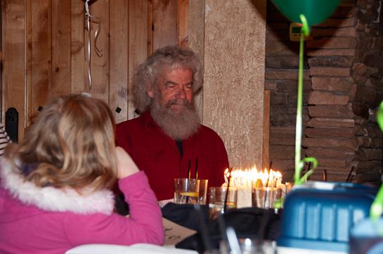Friends and family gather around a table filled with candles and drinks in a rustic setting.