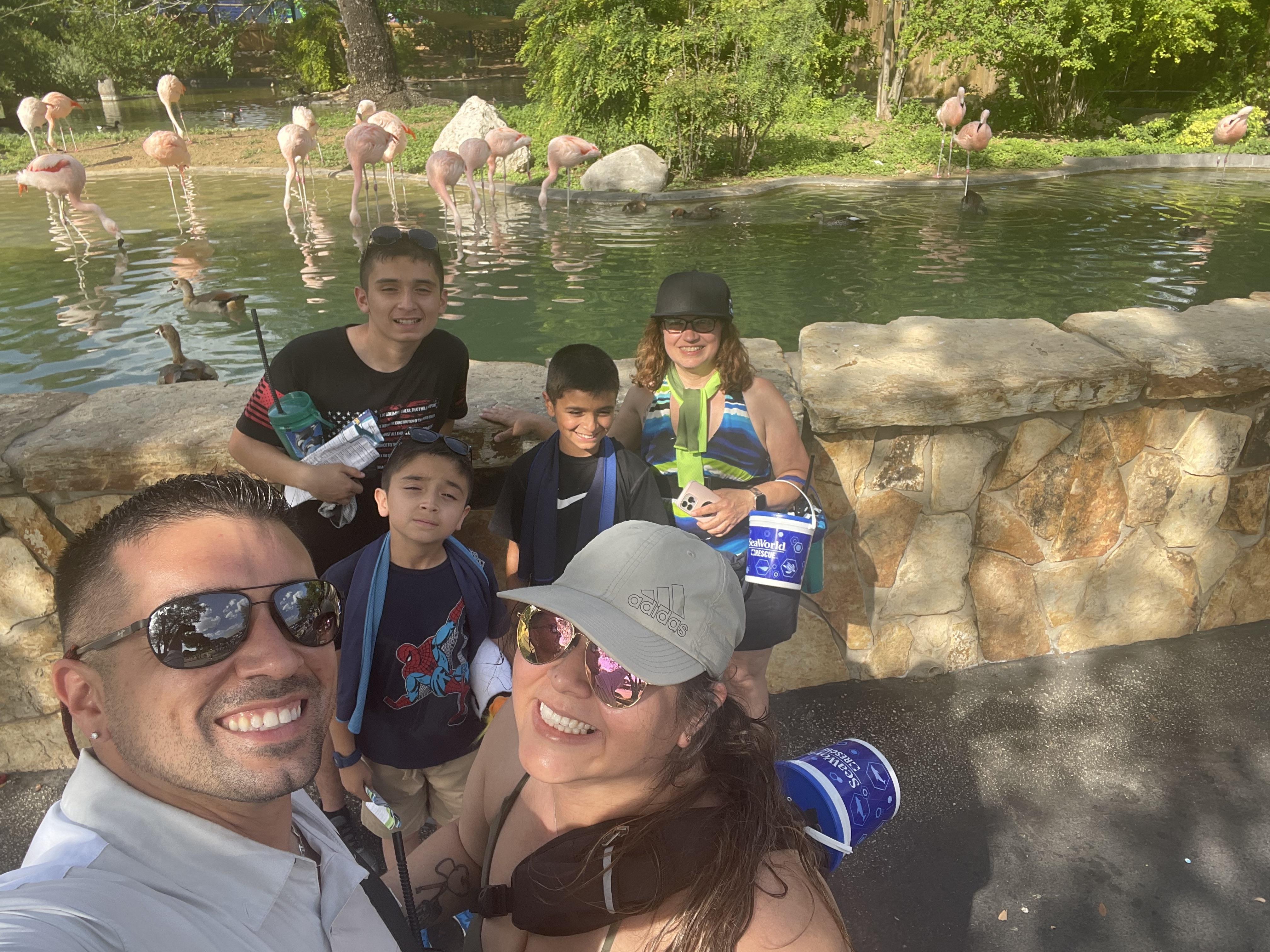 A family poses for a cheerful selfie by the flamingo pond during a sunny day at the park.