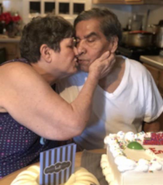 A couple joyfully shares a kiss over a decorated cake during a home celebration.