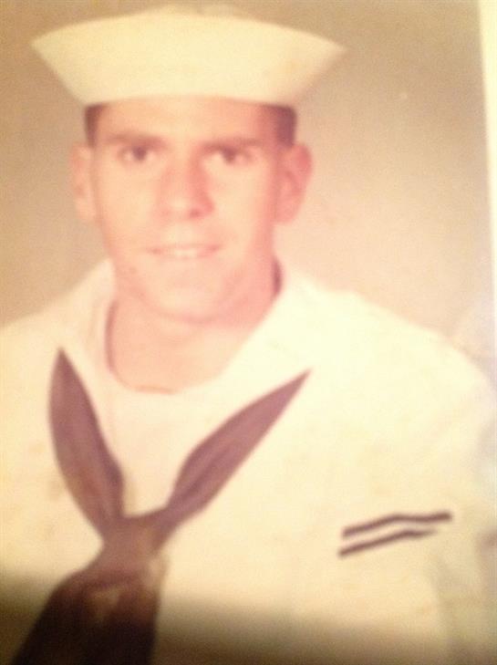 A young sailor smiles warmly while dressed in his naval uniform, presenting a proud moment.