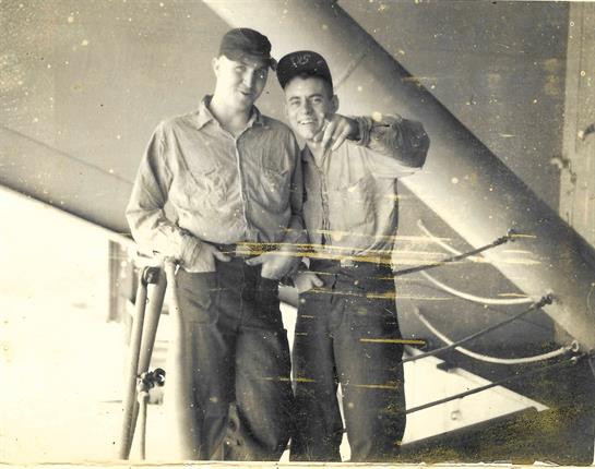 Two young men in uniform smile while standing by an aircraft at an airfield, capturing a moment.
