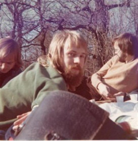 Friends gather on a picnic blanket among trees, sharing food and laughs in the cool air.