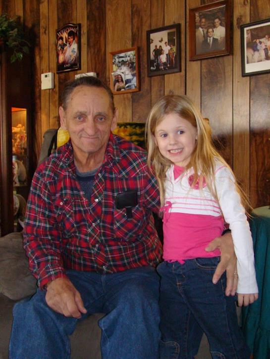 A grandfather and his granddaughter sit together, smiling happily in a warm, inviting home.