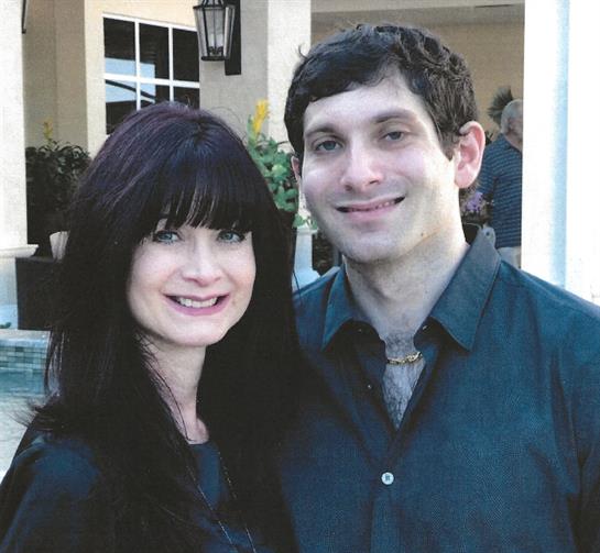 Couple stands side by side, both smiling, dressed in casual clothes on a bright day.
