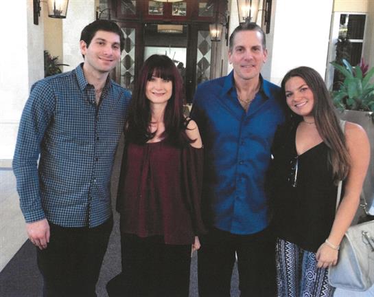 Four friends stand together, smiling cheerfully in front of a beautifully lit entrance at night.