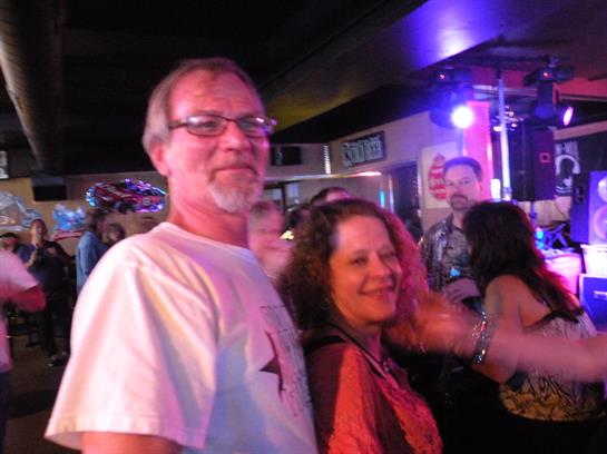 Two people dance and smile in a bustling atmosphere filled with colorful lights and energy.