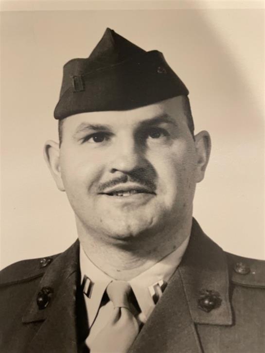 A soldier poses for a portrait wearing a military uniform, displaying rank insignia on his chest.